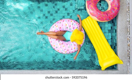 Woman relaxing on donut lilo in the pool at private villa. Inflatable ring and mattress. Summer holiday idyllic. High view from above.