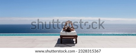 Woman relaxing on lounge chair at poolside overlooking ocean