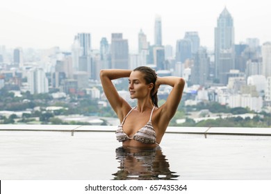 Woman Relaxing On A Rooftop Pool With A Beautiful City View On Background