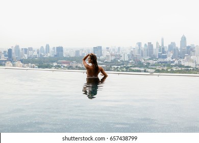 Woman Relaxing On A Rooftop Pool With A Beautiful City View On Background