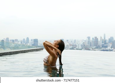 Woman Relaxing On A Rooftop Pool With A Beautiful City View On Background