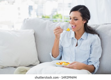 Woman Relaxing On The Sofa Eating Fruits Salad In Her Living Room