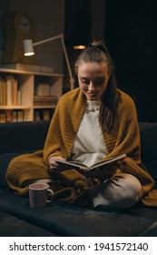 woman relaxing on sofa and reading book. evening moody ambience. she is enjoying time during weekend - Shutterstock ID 1941572140