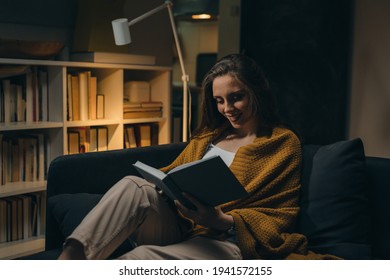 woman relaxing on sofa and reading book. evening moody ambience. she is enjoying time during weekend