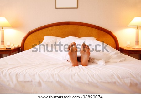 Woman relaxing on soft big bed with white sheets; focus on feet