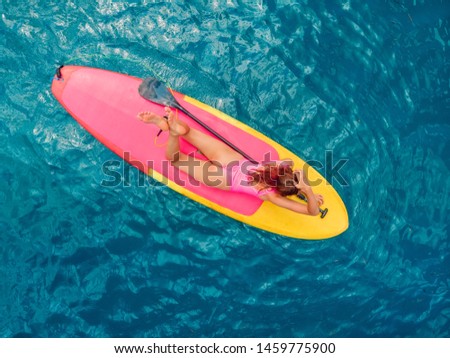 Woman relaxing on stand up paddle board on a quiet blue sea 