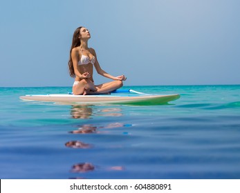 Woman relaxing on a SUP boarding in the sea in a lotus pose. Paddle Board Yoga. Healthy lifestyle in harmony with nature.