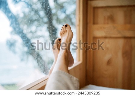 woman relaxing on window sill at home. beautiful female feet with painted nails