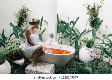 Woman Is Relaxing In Outdoor Bath With Flowers In Bali Spa Hotel.