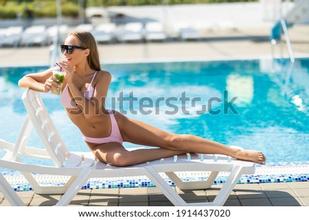 Woman relaxing at the poolside with pina colada cocktail