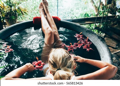 Woman relaxing in round outdoor bath with tropical flowers. Organic skin care in kawa hot bath in luxury spa resort. - Shutterstock ID 565813426