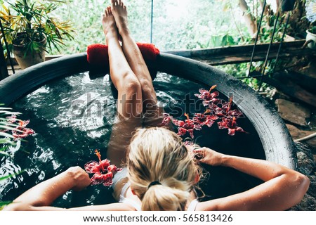 Woman relaxing in round outdoor bath with tropical flowers. Organic skin care in kawa hot bath in luxury spa resort.