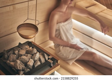 Woman relaxing in wellness spa, sweating in Finnish sauna, focus on sauna stove.
