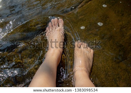 Woman relaxing.Dipping feet in water with rock at the background.