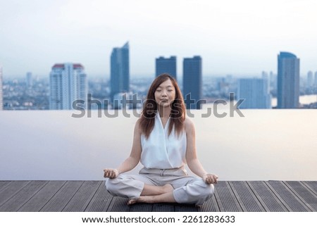 Woman relaxingly practicing meditation at the swimming pool rooftop with the view of urban skyline building to attain happiness from inner peace wisdom