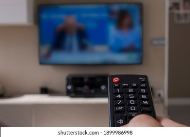 The woman with the remote control in hand watches the sports channel and presses the button on the remote control. First remote control in hand. Selective focus