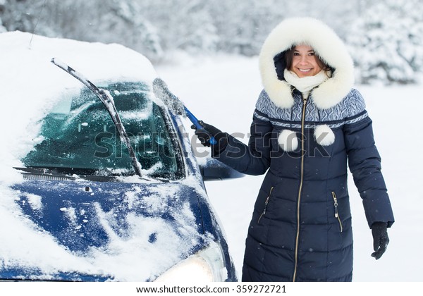 Woman remove\
snow from windshield with snow\
brush.