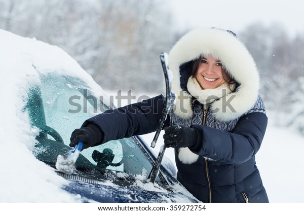 Woman remove\
snow from windshield with snow\
brush.