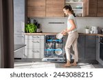 A woman removes clean ceramic dishes from the dishwasher. Household and useful technology concept. High quality photo. 