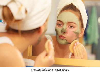 Woman removing facial dried clay mud mask with sponge in bathroom in front of mirror. Skin care. Girl taking care of her complexion. Beauty spa treatment.