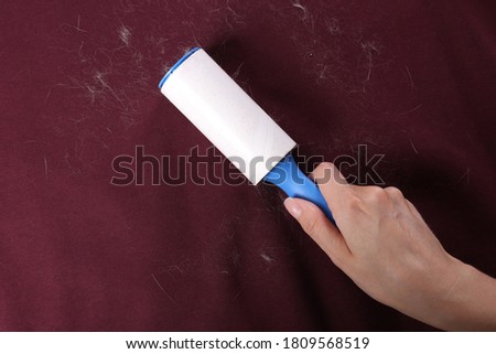 Woman removing hair from red fabric with lint roller, closeup