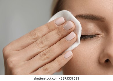 Woman removing makeup with cotton pad on grey background, closeup - Powered by Shutterstock