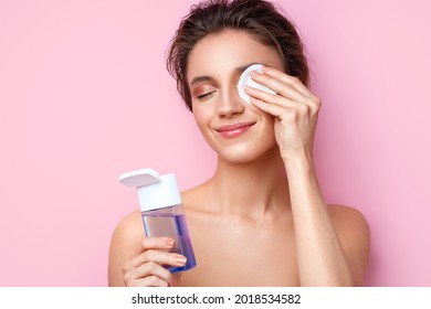 Woman removing makeup, holds cotton pads near face. Photo of woman with perfect skin on pink background. Beauty and skin care concept