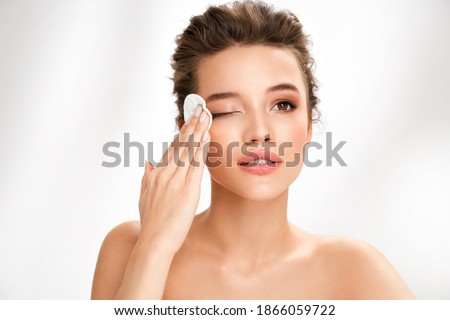 Woman removing makeup, holds cotton pads near face. Photo of woman with perfect skin on white background. Beauty and skin care concept
