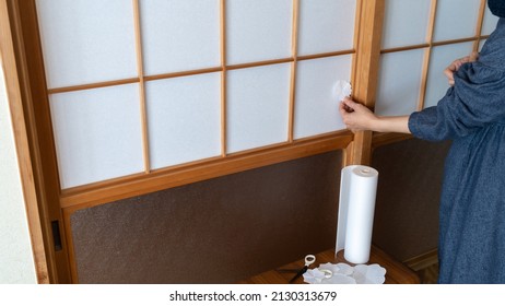 A woman repairing a torn shoji. Sliding door in a Japanese room.