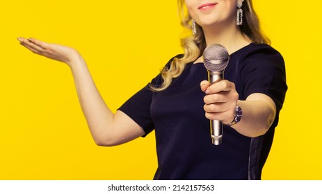 woman, reporter, TV presenter holding microphone isolated bright yellow background. Focus on mic