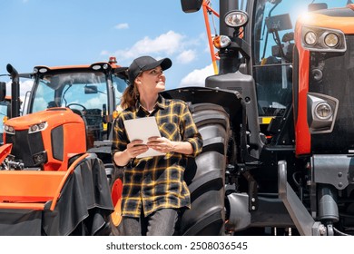 Woman representative at a dealership for construction and agricultural machinery stands next to a tractor holds digital tablet and smiling. - Powered by Shutterstock