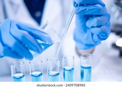 Woman research scientist biology chemistry medicine pouring liquid from beaker to test tube indoor science laboratory room, adult female person blue glove work discovery experiment medical chemist - Powered by Shutterstock