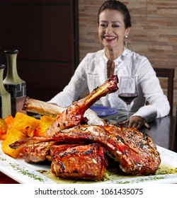 Woman In Restaurant Drinking Red Wine And Eating Rack Of Roasted Lamb