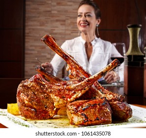 Woman In Restaurant Drinking Red Wine And Eating Rack Of Roasted Lamb