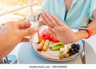Woman in a restaurant refuses the offered salt and pepper shaker with a gesture of her hand. Diet for gout and high cardiovascular blood pressure