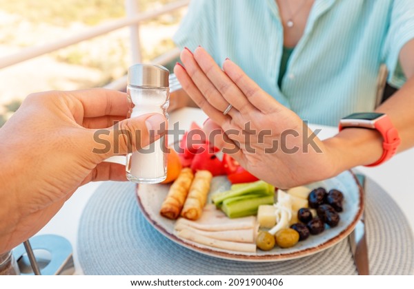 Woman in a restaurant refuses the offered salt\
and pepper shaker with a gesture of her hand. Diet for gout and\
high cardiovascular blood\
pressure