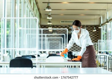 Woman Restaurant Staff Cleaning Table With Alcohol Spray Wearing Glove, Face Shield And Mask Before Open The Restaurant