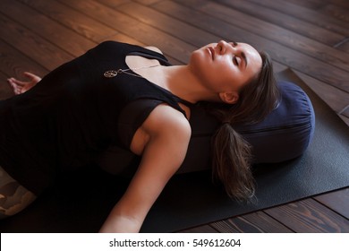 Woman resting after a yoga class in shavasana. Under back her bolster  for spine therapy