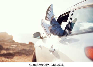 woman resting in the car with sneakers out of the window at sunset