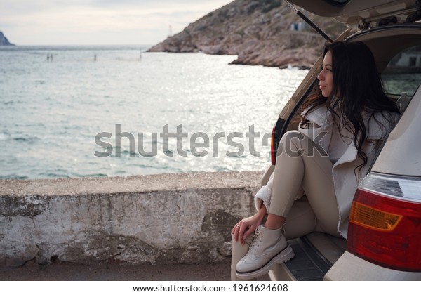 A woman\
resting inside the trunk of a car and looking out to sea. Autumn\
ride at sunset. The concept of freedom of movement. Autumn weekend.\
Traveling alone or solo travel\
concept.