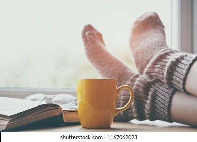 Woman resting keeping legs in warm socks on table with morning coffee and reading book - Powered by Shutterstock