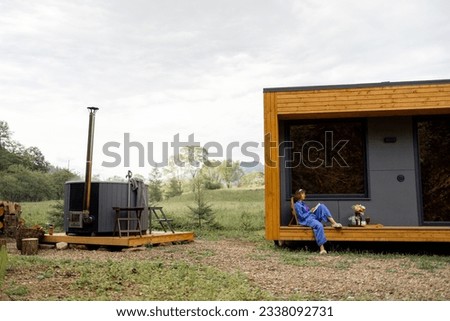 Woman resting on nature in wooden house with a hot tub nearby. Concept of recreation and escaping to nature
