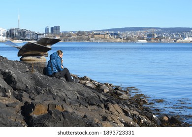 A Woman Resting On The Rocks . Outdoor View Of Central Oslo From The Bank Of Bygdøy Peninsula. Spring In Norway. 
