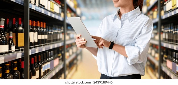 Woman retail sales manager analysing commercial performance of alcohol department in supermarket. Female employee using digital tablet in liquor store. - Powered by Shutterstock