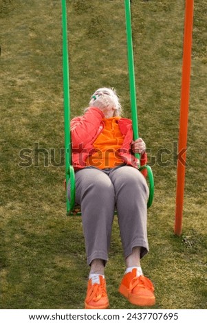 a woman of retirement age rides on a children's swing and eats a cake