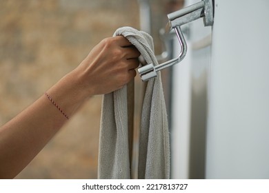 A woman retrieves white towels from a holder in a hotel bathroom adorned with textured and white walls. - Powered by Shutterstock