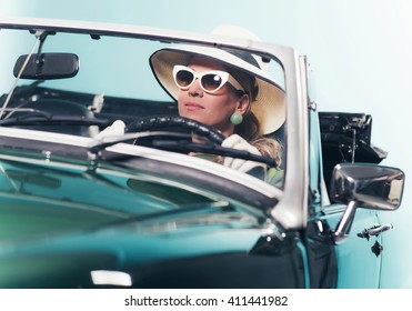 Woman In Retro 1960s Fashion With Hat And Shades Driving Convertible.