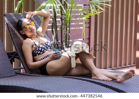 Woman in retro bikini lying on a deckchair.  Hides her face from the sun shine.