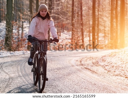 A woman rides a bike in winter. Concept of cycling during snowy weather. Snow and sun weather in the park