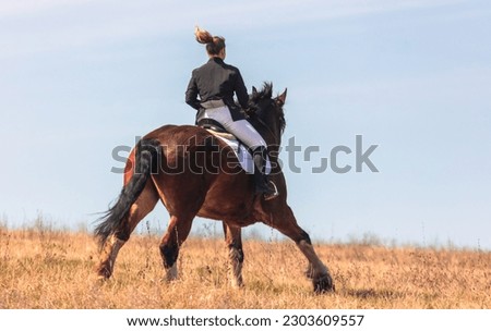 A woman rides a horse against a blue sky.